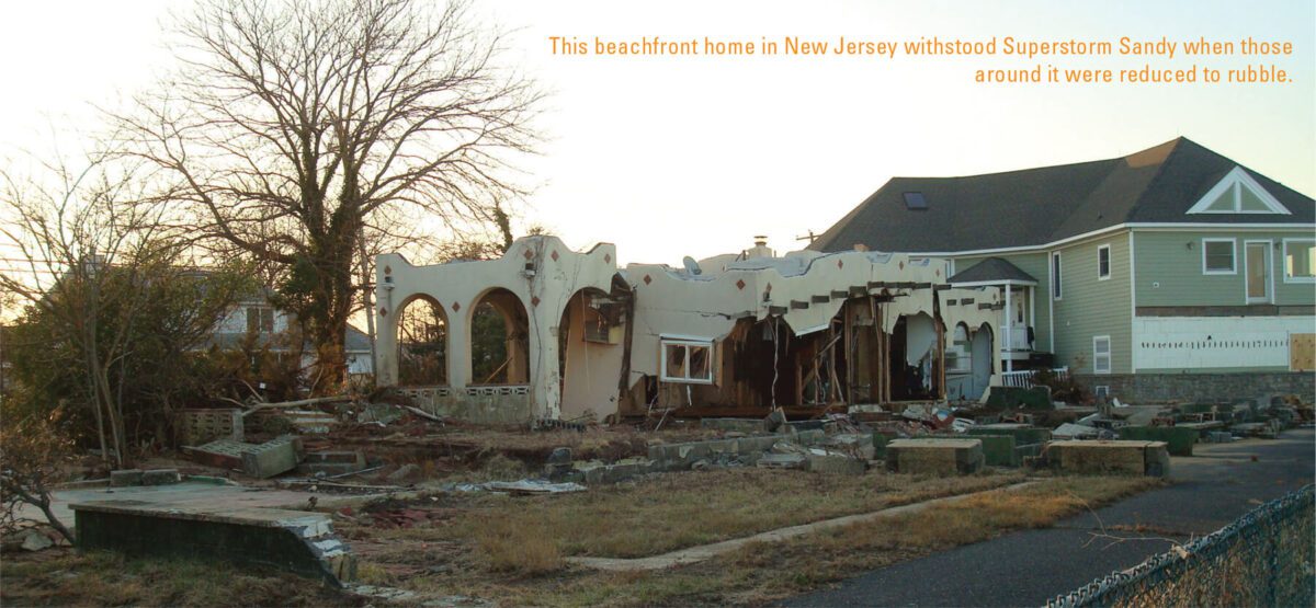 A lone standing beachfront home in New Jersey shows severe damage from Superstorm Sandy, partially destroyed with missing walls and debris scattered around. Surrounding houses and structures are reduced to rubble. Nearby, a larger, newer home appears intact.